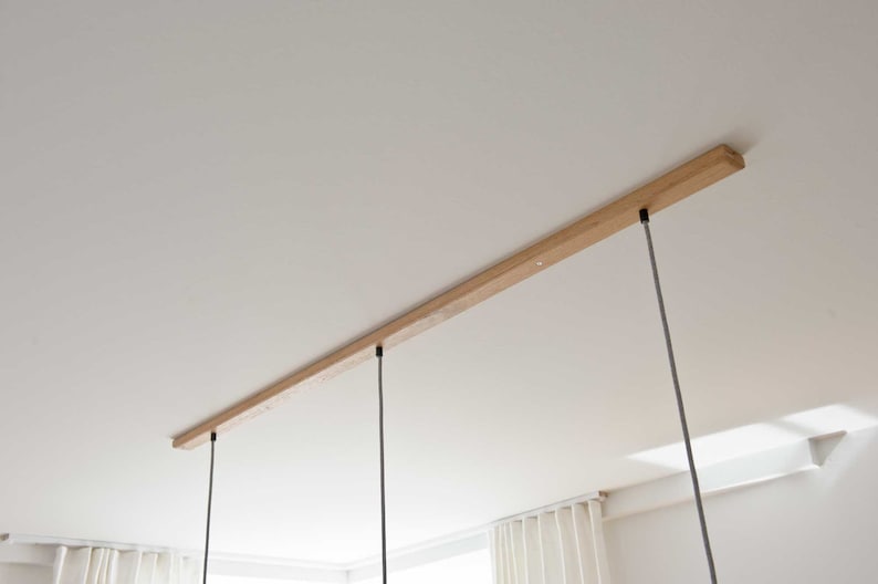 May include: A wooden ceiling track with three black cords hanging down from it. The cords are attached to the track with black metal fixtures.