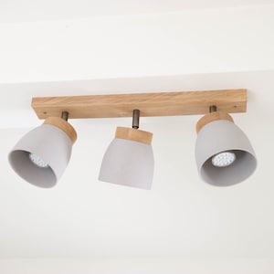 May include: A three-light ceiling fixture with a wooden base and grey fabric shades. The shades are round and have a slight curve at the bottom.