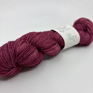 May include: A skein of burgundy yarn with a label that reads "Red Wine" and features a cactus illustration. The yarn is a deep, rich shade of red, perfect for knitting or crocheting projects.