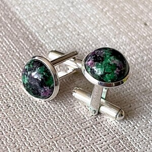 May include: A pair of silver cufflinks with green and pink gemstone cabochons. The cabochons have a mottled pattern.