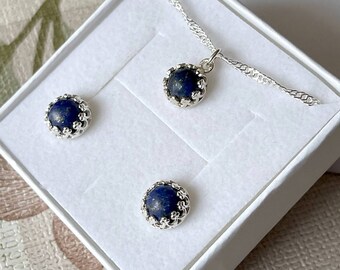 May include: A set of lapis lazuli earrings and a necklace. The earrings and pendant feature a round blue stone with a silver floral design.