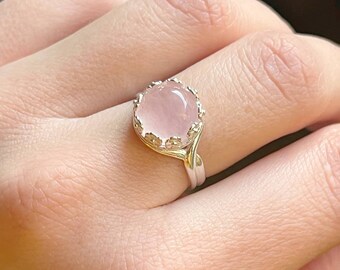 May include: A silver ring featuring a delicate floral design and a pink oval gemstone.