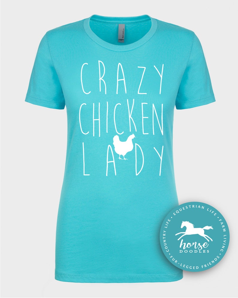 Peut inclure: Un t-shirt turquoise avec l'inscription blanche "CRAZY CHICKEN LADY" et un dessin de poulet blanc. Le t-shirt a un col rond et des manches courtes. Un logo circulaire avec un cheval est dans le coin inf&eacute;rieur droit.