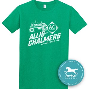May include: A green t-shirt featuring a white graphic of a tractor and the text "ALLIS-CHALMERS ESTABLISHED 1901". The shirt also has the letters "AC" inside a diamond shape. A circular logo with a horse is in the bottom right corner.