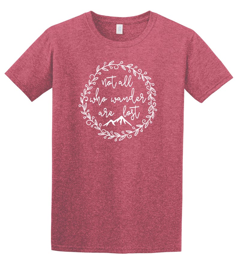 以下が含まれることがあります： 白い円形デザインの赤いTシャツ。デザインは、下部に山のイラストが付いた、装飾的なフォントで「not all who wander are lost」というテキストを特徴としています。シャツは半袖とクルーネックです。