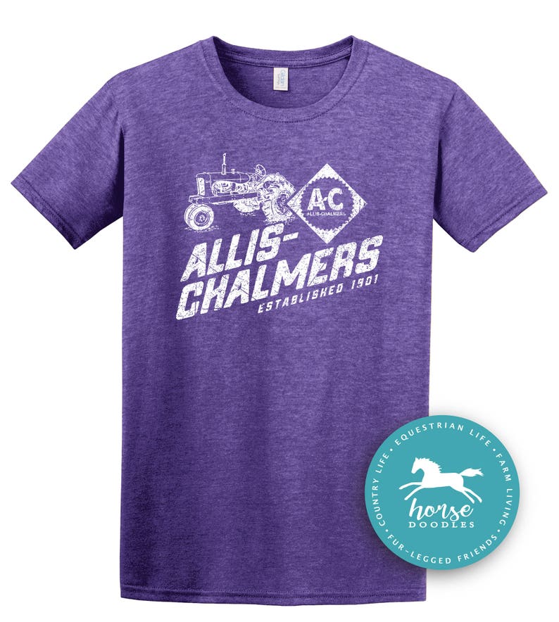 May include: Purple t-shirt with a white graphic of a tractor and the words "ALLIS-CHALMERS ESTABLISHED 1901". A round sticker with a horse graphic is on the bottom right. The shirt is a crew neck.