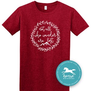 以下が含まれることがあります： 白い花のリースの中に「not all who wander are lost」というテキストが入った、マルーン色のTシャツ。馬のグラフィックと「horse doodles」という言葉が入った円形のロゴが右下にあります。