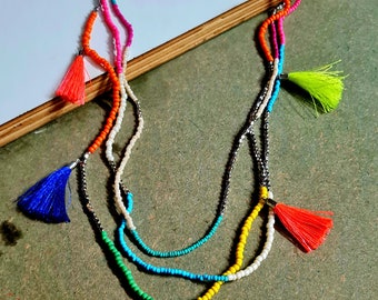 May include: A multi-strand necklace with colorful beaded strands and tassel pendants. The necklace features strands of green, blue, white, orange, pink, and yellow beads. Each strand has a tassel pendant in a matching color.