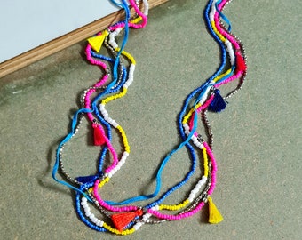 May include: Multi-strand necklace with colorful beads and tassels. The necklace features blue, pink, yellow, white, and silver beads, and has tassels in blue, pink, yellow, and red.