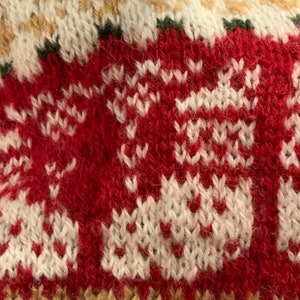 May include: Close-up of a red and white knitted fabric with a repeating pattern. The fabric has a fuzzy texture and is made of wool.