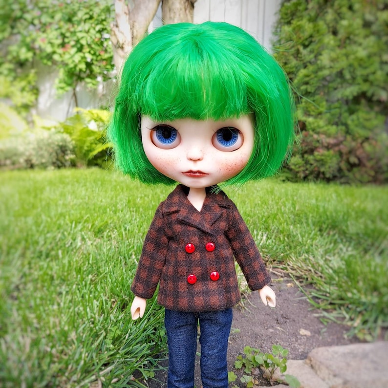 May include: A doll with bright green hair, blue eyes, and a brown and red plaid jacket. The doll is wearing blue jeans and has a neutral expression.