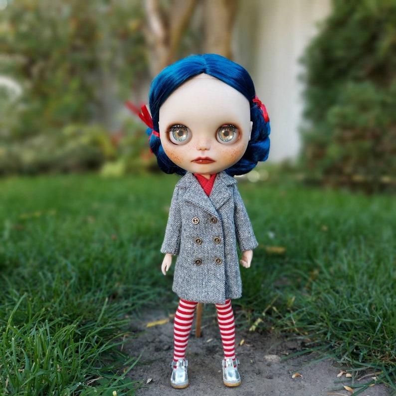 May include: A doll with blue hair, wearing a gray coat, red and white striped tights, and silver shoes. The doll has blue eyes and red lips.