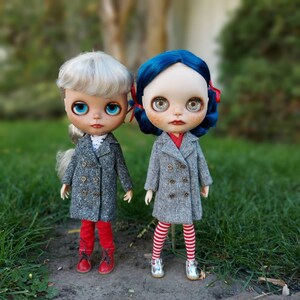 May include: Two dolls wearing gray coats with red and white striped pants and red shoes. The doll on the left has blonde hair and blue eyes. The doll on the right has blue hair and blue eyes.