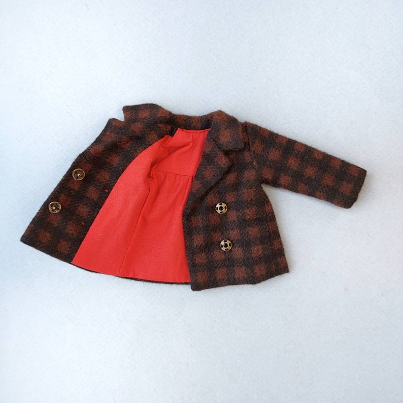 May include: A brown and black plaid coat with a red lining and gold buttons. The coat is open and the lining is visible.