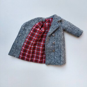 May include: A gray tweed coat with a red and white plaid lining. The coat has a double breasted closure and silver buttons.
