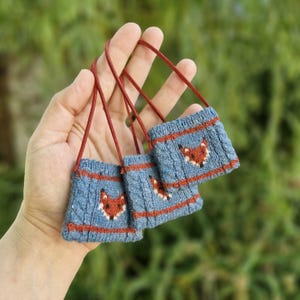 May include: Three small blue knitted bags with red straps and fox faces embroidered on the front.