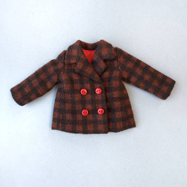 May include: A brown and black plaid coat with red buttons. The coat has a double breasted closure and a collar.