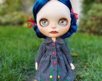 May include: A doll with blue hair and a gray coat with red buttons and embroidered flowers. The doll has blue eyes and freckles.