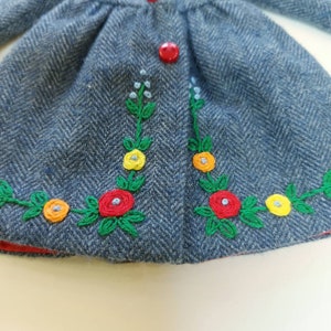 Puede incluir: Una chaqueta vaquera azul con un bot&oacute;n rojo y detalles florales bordados en verde, rojo, amarillo y naranja.