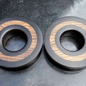 May include: Two black wooden rings with a brown wood inlay. The rings have a large hole in the centre.
