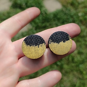 May include: Two round wooden earrings with a black and gold design. The top half of each earring is black, and the bottom half is gold.