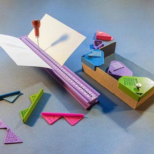 Puede incluir: Una herramienta de encuadernación de color morado con una hoja de papel blanca que se está perforando. La herramienta tiene una regla con los números del 1 al 59. También hay cinco herramientas de plástico de diferentes colores con los números 1.5, 2, 2.0, 2.5 y 3.0.