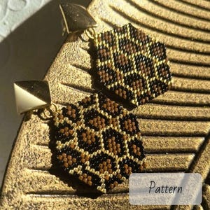 Op de afbeelding: Goudkleurige oorstekers met een geometrisch, zeshoekig ontwerp. De oorbellen hebben een patroon van bruine, zwarte en gouden kralen, met een gouden vierkante stud. Het woord "Pattern" is zichtbaar.