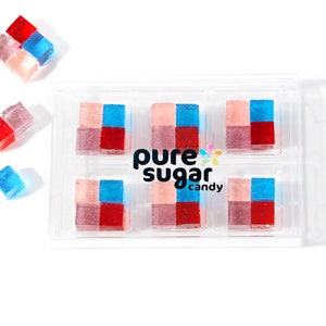 May include: A clear plastic tray filled with six red, blue, and pink layered square candies. The candies are arranged in a 2x3 grid. The tray has the words "pure sugar candy" printed on the bottom. There are three additional candies outside of the tray.