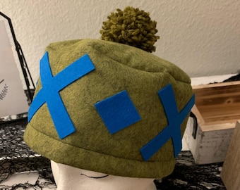 May include: A green felt hat with a blue X pattern and a green pom-pom on top.