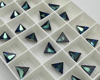 May include: A collection of iridescent, triangular-shaped rhinestones arranged in a white grid. The rhinestones have a dark blue and green color, with a metallic silver backing. The arrangement suggests they are for crafting or jewelry making.