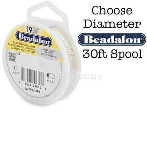 Puede incluir: Un carrete de hilo para ensartar cuentas Beadalon, de color plateado. La etiqueta dice "Choose Diameter" y "30ft Spool". El carrete es blanco con una etiqueta amarilla y azul. El hilo es para ensartar cuentas.