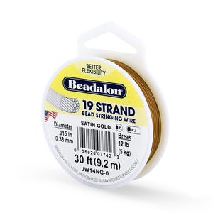 Puede incluir: Un carrete de hilo para ensartar cuentas Beadalon de 19 hebras, oro satinado. La etiqueta indica un diámetro de 0,38 mm, una resistencia a la rotura de 5 kg y una longitud de 9,2 m. El carrete es blanco con una etiqueta amarilla y azul.