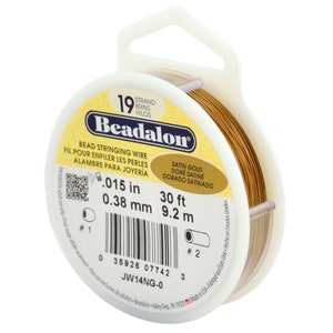 May include: A spool of Beadalon bead stringing wire in satin gold. The package indicates the wire is .015 inches in diameter and 30 feet long. The label also includes the text "BEAD STRINGING WIRE" and "SATIN GOLD".