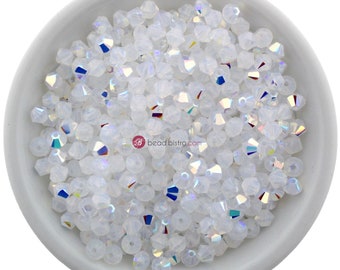 May include: A bowl filled with white iridescent glass beads. The beads are small and have a faceted shape. The beads are in a white bowl.