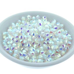 May include: A bowl filled with iridescent white crystal beads. The beads are faceted and have a rainbow sheen.
