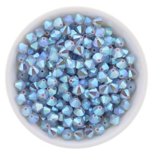May include: A white bowl filled with light blue iridescent glass beads. The beads are faceted and have a pointed shape.