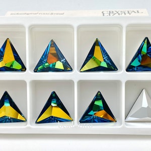 Puede incluir: Un conjunto de ocho cristales de imitación triangulares en una bandeja blanca. Los cristales de imitación son azul, verde y amarillo iridiscentes. Un cristal de imitación es transparente.