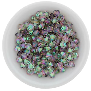 May include: A collection of iridescent crystal beads in a white bowl. The beads have a multifaceted design, reflecting a spectrum of colors including green, purple, and gold. Ideal for jewelry making and crafting.