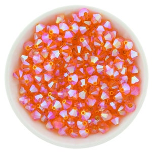 May include: A bowl filled with orange iridescent glass beads. The beads are faceted and have a shiny finish.