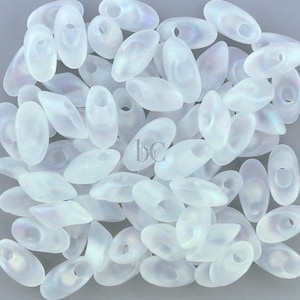 May include: A collection of white opaque glass seed beads with a hole in the center. The beads are oval shaped and have a slightly iridescent finish.