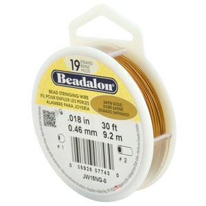 Könnte beinhalten: Eine Spule Beadalon-Perlenschnur in Satin-Gold. Die Verpackung weist 9,2 m Draht mit 0,46 mm Durchmesser auf. Das Etikett enthält auch "BEAD STRINGING WIRE" auf Englisch, Französisch und Spanisch.