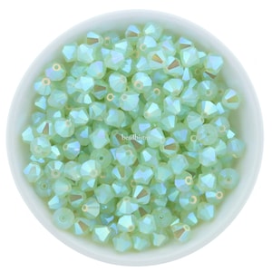 May include: A bowl filled with light green iridescent glass beads. The beads are faceted and have a shiny finish.