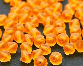 Puede incluir: Primer plano de un montón de cuentas de vidrio naranja. Las cuentas son facetadas y tienen un acabado brillante.