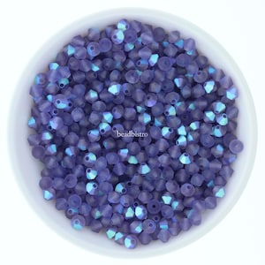 May include: A bowl of small, iridescent purple glass beads. The beads have a faceted, conical shape and are arranged in a random pattern.