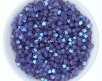 Pode incluir: Uma tigela de pequenas contas de vidro roxo iridescentes. As contas têm uma forma cónica facetada e estão dispostas em um padrão aleatório.