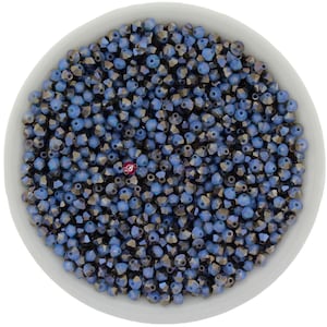 Pode incluir: Uma tigela branca cheia de pequenas contas facetadas em tons de azul e cinza. As contas têm uma qualidade reflexiva e iridescente, criando um efeito brilhante. As contas estão espalhadas por toda a tigela.