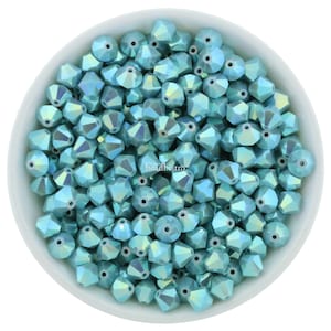 May include: A bowl filled with light blue iridescent glass beads. The beads are faceted and have a shiny finish.