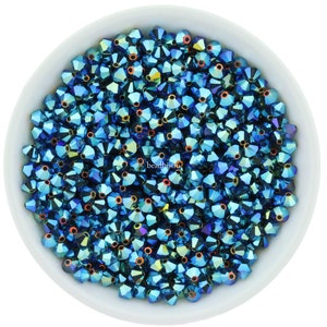 Puede incluir: Un bol lleno de cuentas de vidrio azul verdoso iridiscente. Las cuentas son facetadas y tienen un brillo met&aacute;lico.