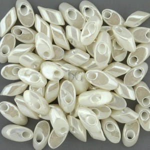May include: A pile of white oval-shaped glass beads with a hole in the center. The beads have a pearlescent finish.