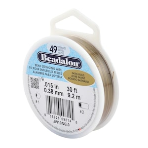 Op de afbeelding: Een spoel Beadalon kralenrijgdraad in satijngoud. Het etiket geeft aan dat de draad 0,38 mm in diameter is en 9,2 m lang. De spoel is wit met blauwe en gouden accenten.